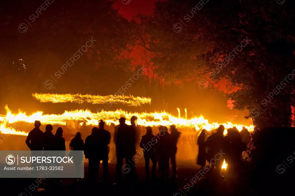 Silhouttes Of People Watching Procession Of Bonfire Societies With Burning Torches Coming Down Country Lane With Sky Lit By Red Flares On Bonfire Nigh...