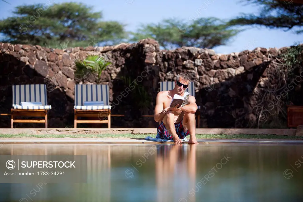 Shaba National Reserve; Kenya, Guest relaxing reading book beside swimming pool at luxurious Joy's Camp