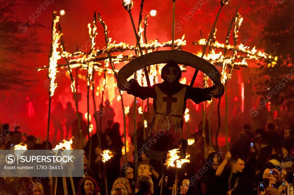 People Dressed As Monks Carrying Southover Bonfire Society Banner And Burning Crosses Lit From Behind By Red Flare On Bonfire Night, Lewes, East Susse...