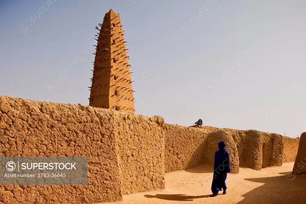 Niger, Sahara Desert, Agadez Region, Veiled Tuareg Man Walking Past Agadez Grand Mosque; Agadez