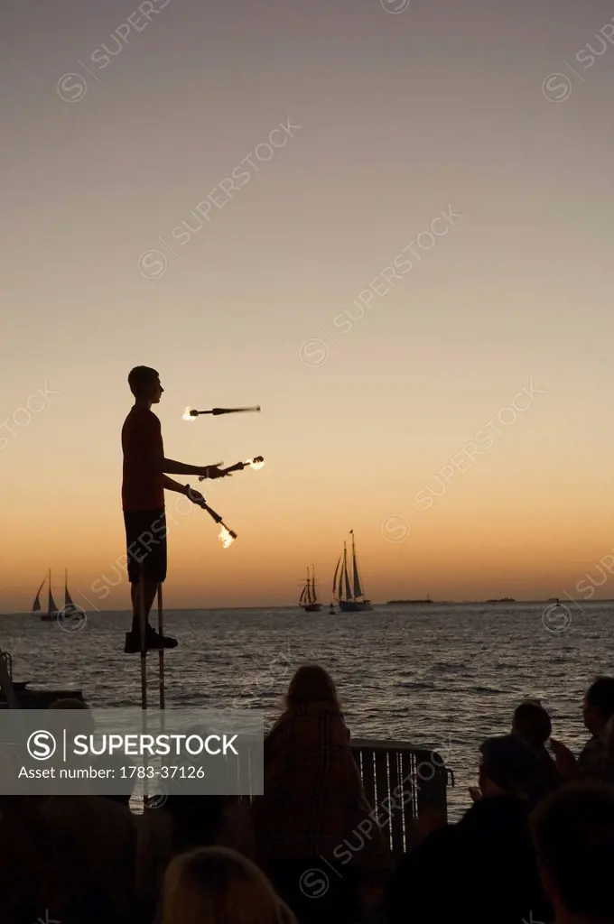 Juggler using lighted torches entertains crowd who have come to watch sunset at Mallory Square; Key West, Florida Keys, USA