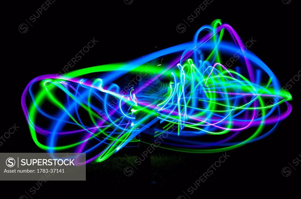 Woman spinning hula hoop lit with LEDs in field at night; West Sussex, UK
