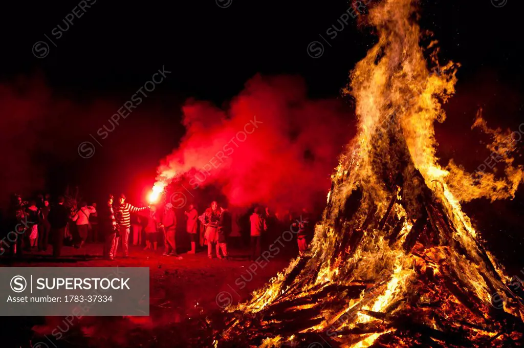 Man with red flare beside large bonfire at Battle Bonfire Night; East Sussex, England, UK
