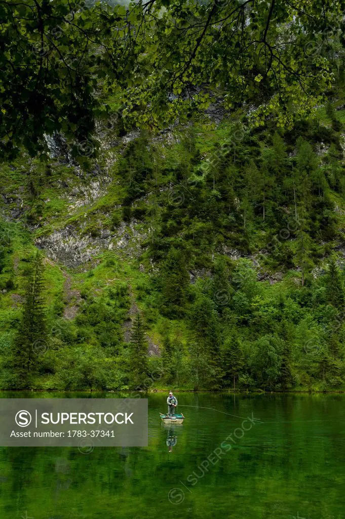 Man fly fishing from small boat in Lake Forggensee near Ruhpolding; Bavaria, Germany