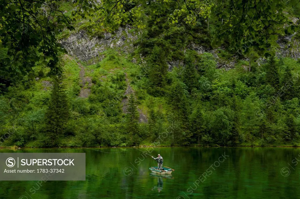 Man fly fishing from small boat in Lake Forggensee near Ruhpolding; Bavaria, Germany