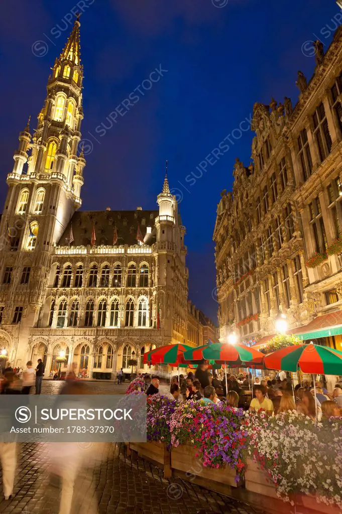 People eating and drinking at cafe tables at dusk in Grand Place; Brussels, Belgium