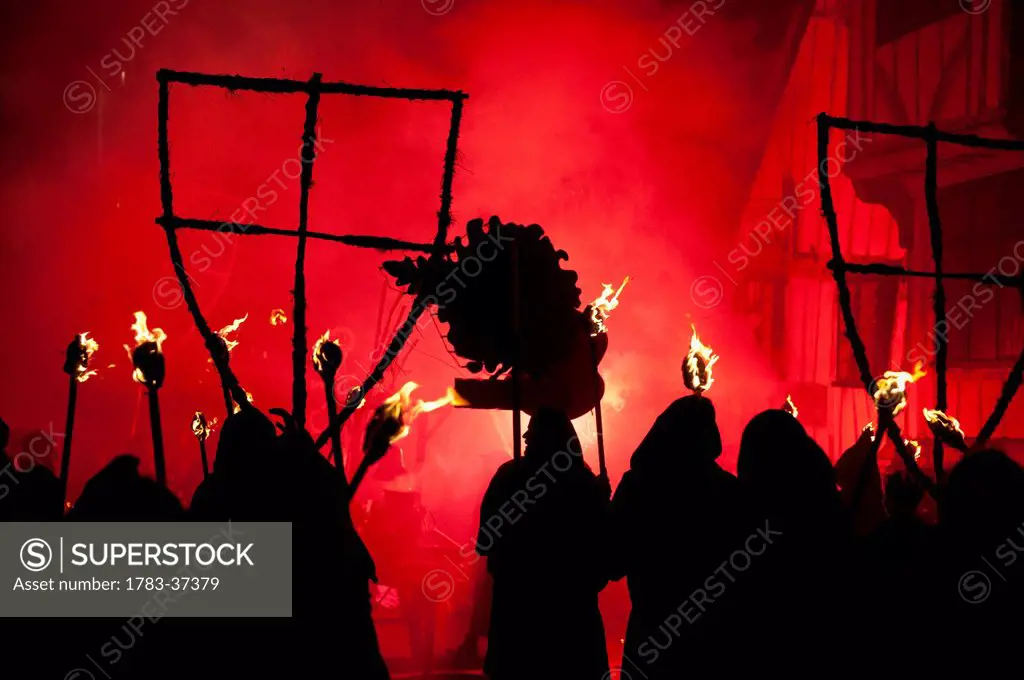 Silhouettes of monks from Southover Bonfire Society lit by red flares on United Grand Procession down High Street, Bonfire Night; Lewes, East Sussex, ...