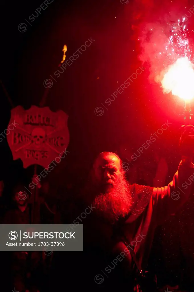 Man with red flare in front of banner for Battel Bonfire Boyes walking in procession along main street of Battle Bonfire Night; East Sussex, England, ...