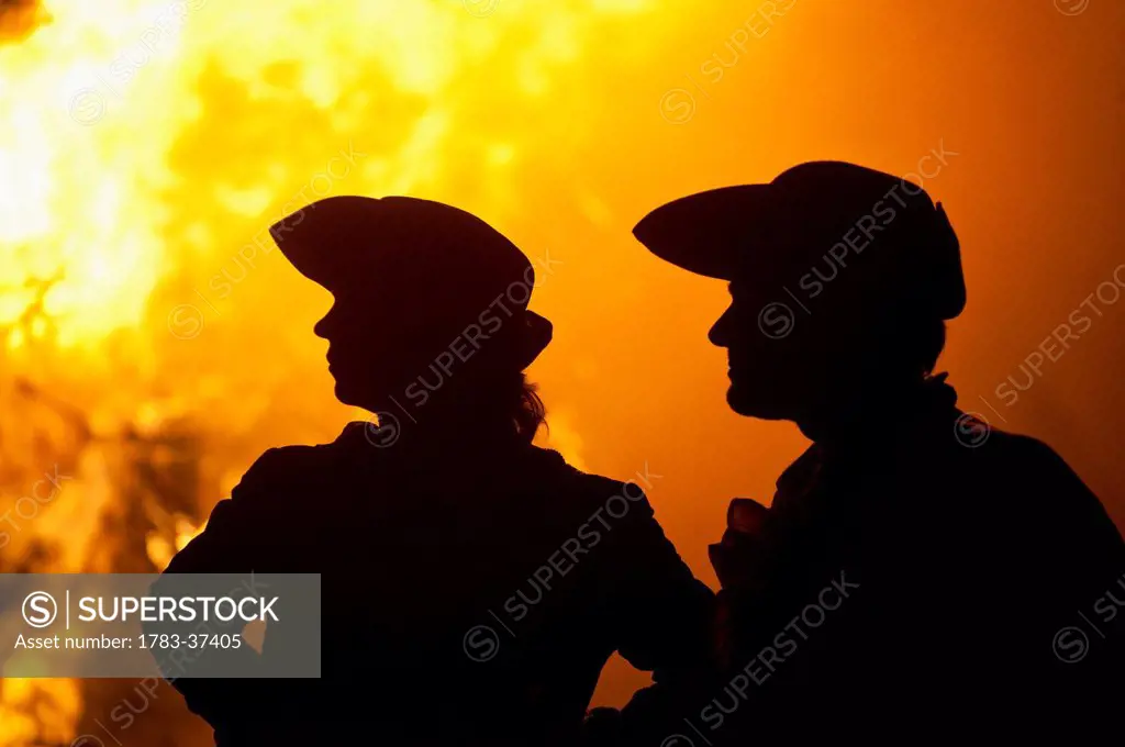 Silhouettes of man and woman dressed as pirates in front of large bonfire; Lewes, East Sussex, UK
