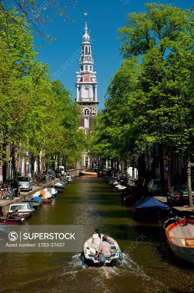 Couple in boat going along canal with spire of Zuiderkerk Church in background; Amsterdam, Holland