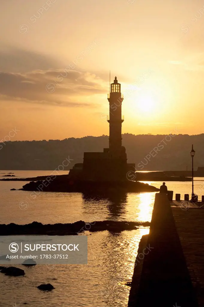 Silhouette of lighthouse at harbor entrance at dawn; Chania, Crete, Greece