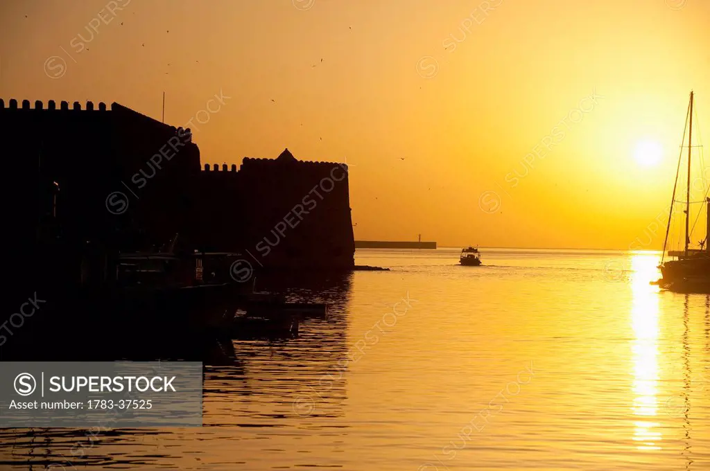 Fishing boat, harbor and Venetian fortress at dawn; Heraklion, Crete, Greece