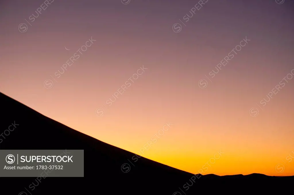 Crescent moon above sand dune at dusk near Merzouga in Sahara Desert; Erg Chebbi, Morocco