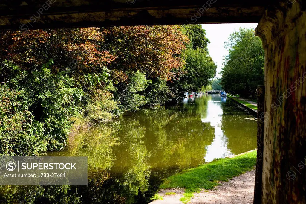 The Grand Union Canal, towpath, barges, and lush green surrounding countryside. viewed from under a bridge; Hemel Hempstead, Hertfordshire, UK