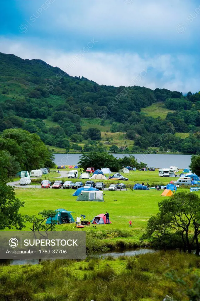 Colorful tents & caravans in the valley, surrounded by hillsides, river and lake, Llyn Gwynant Campsite; Nantgwynant, Snowdonia National Park, North W...