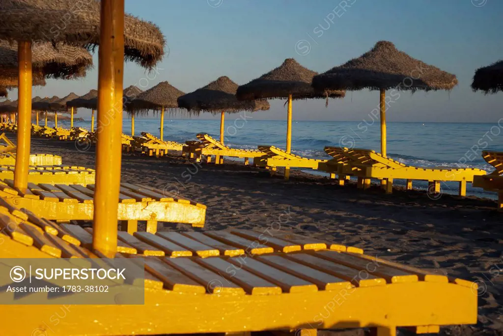 Yellow beach chairs and straw sun umbrellas; Malaga, Spain