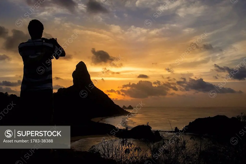 Man taking photograph of Morro do Pico at sunset; Fernando de Noronha, Pernambuco, Brazil