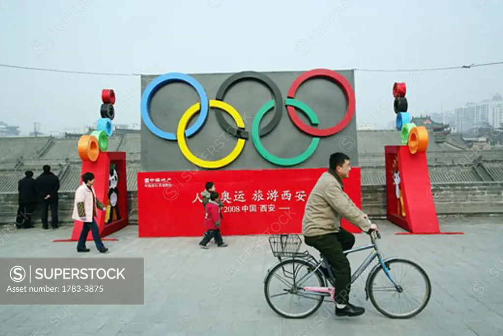 A local man rides past an Olympic display by the Old City wall, Xian, Xi'an, Capital of Shaanxi Province, China 