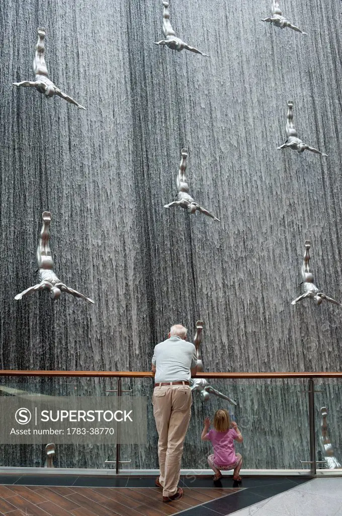 Man and girl looking at large installation of waterfall and divers in Dubai Mall shopping centre; Dubai, UAE