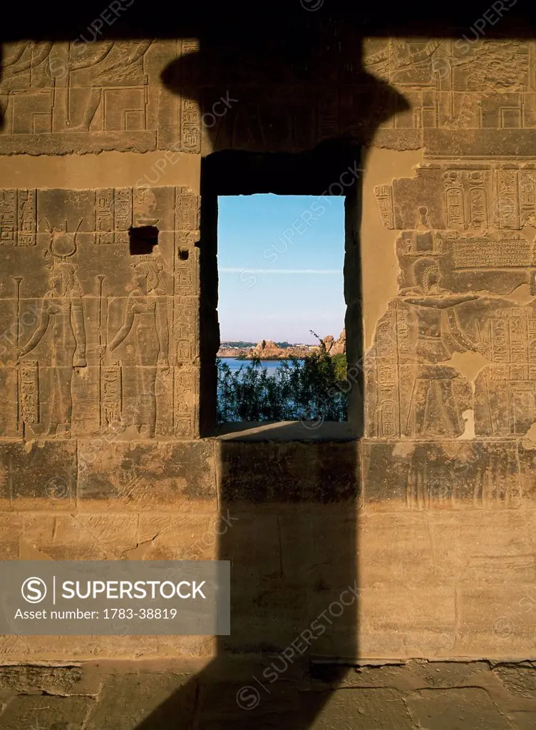 Wall of West Colonnade covered in reliefs and hieroglyphs with shadow of column and window to Lake Nasser, Temple of Isis; Philae Island, Aswan, Egypt