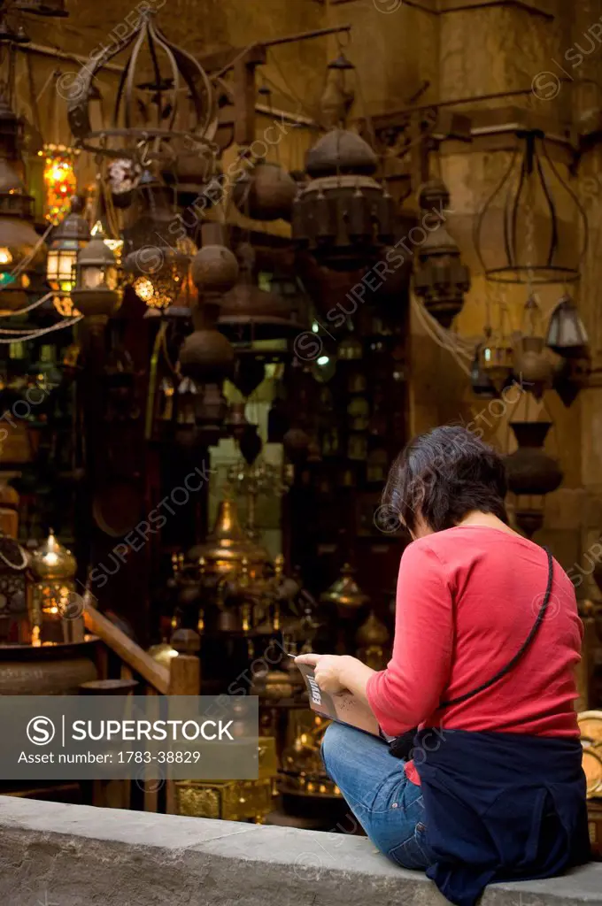 Woman reading guidebook beside stalls in covered gateway in Khan El Khalili; Cairo, Egypt