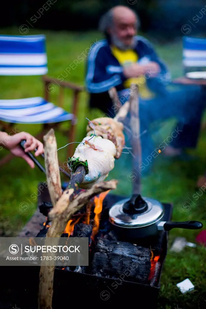 Family camping holiday, spit roast chicken over open fire at Llyn Gwynant Campsite; Nant Ggwynant, Snowdonia National Park, North Wales, Wales, UK