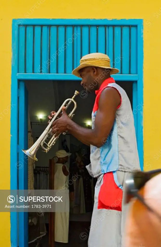 A street entertainer playing a trumpet beside colorful doorway, Havana, Cuba