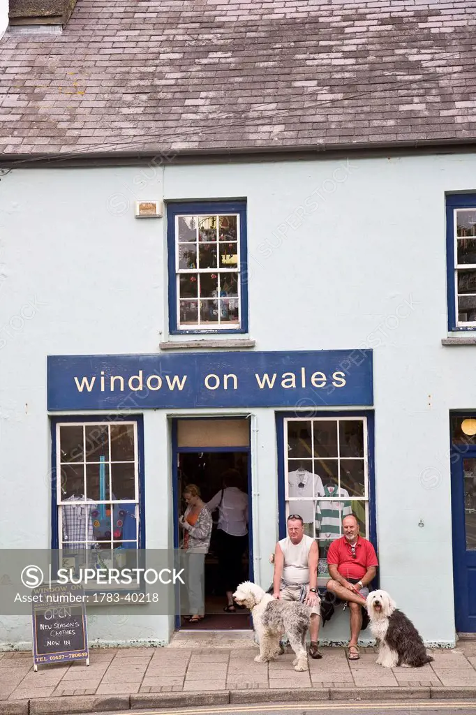 United Kingdom, Wales, Two men with dogs sitting in front of shop; Pembrokeshire