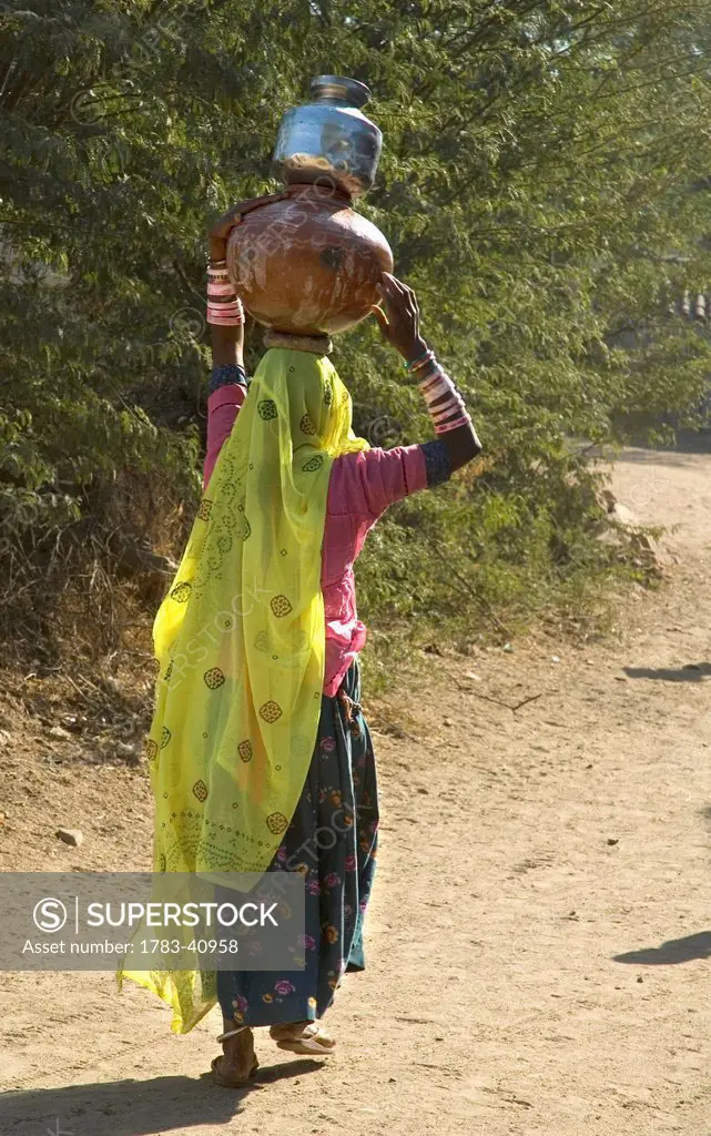 India, Rajasthan, Woman with one terracotta and one tin water pot on her head; Nimaj