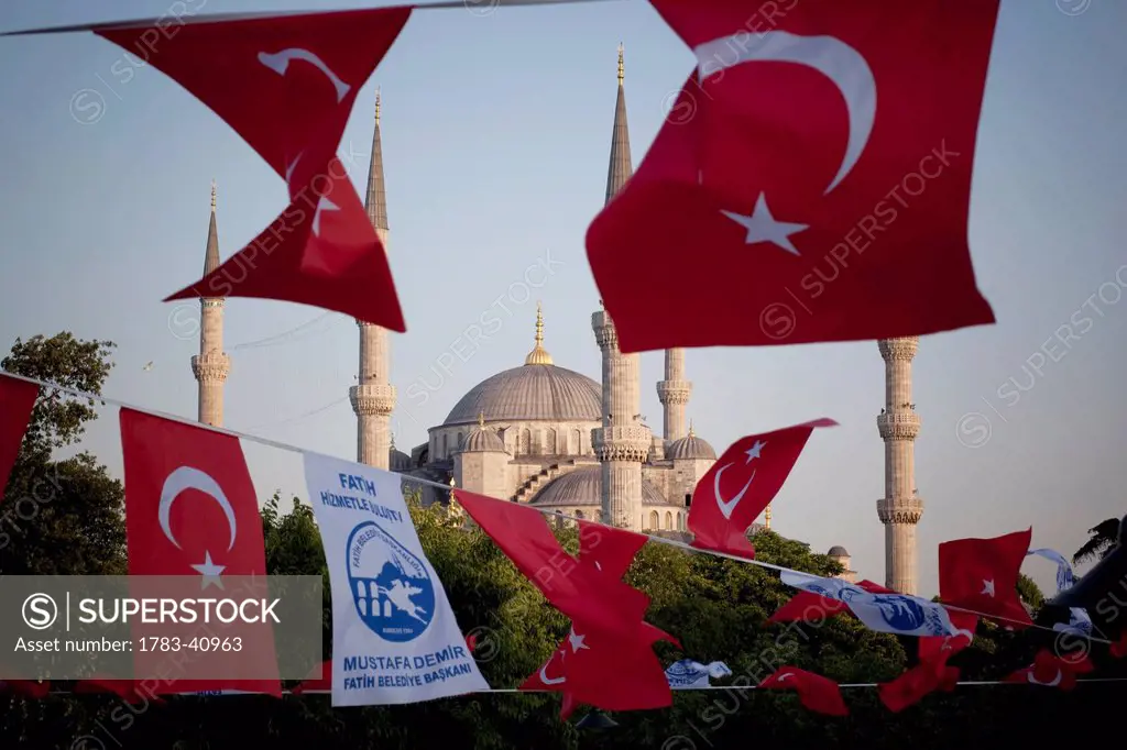 Turkey, Istanbul, Turkish flags flapping in breeze at dusk over Blue Mosque; Sultanahmet