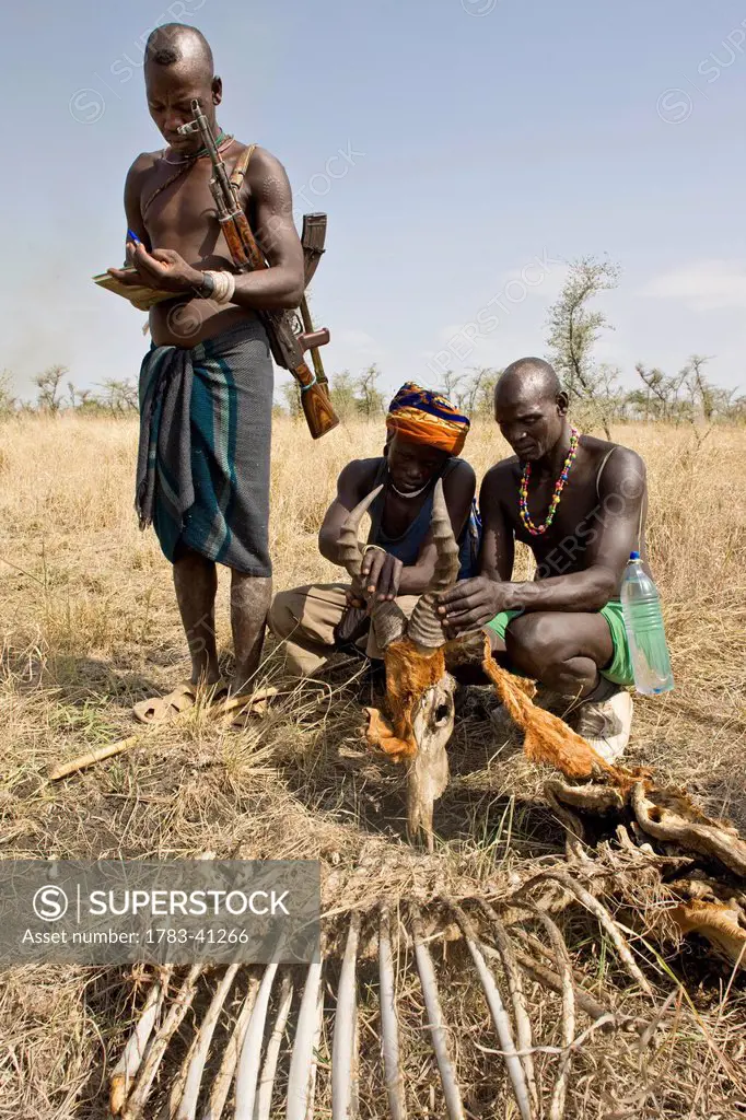 Ethiopia, Southern Nations Nationalities and Peoples' Region, South Omo, Mursi tribal men with remains of topi killed by lion on savanah; Southern Mur...