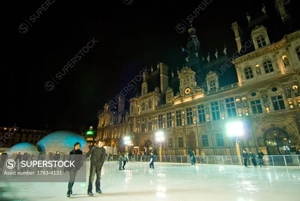 People ice skating in front of the Hotel de Ville at night, Paris, France 