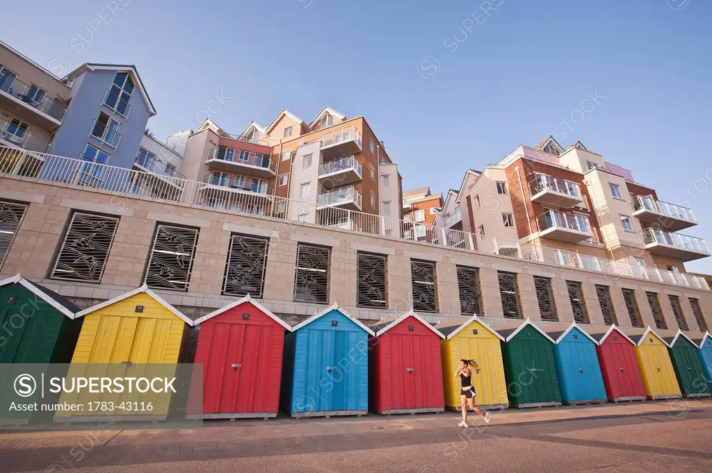 Jogger and colorful beach huts and apartments at Honeycombe Beach development next to Boscombe Pier; Bournemouth, Dorset, England, UK