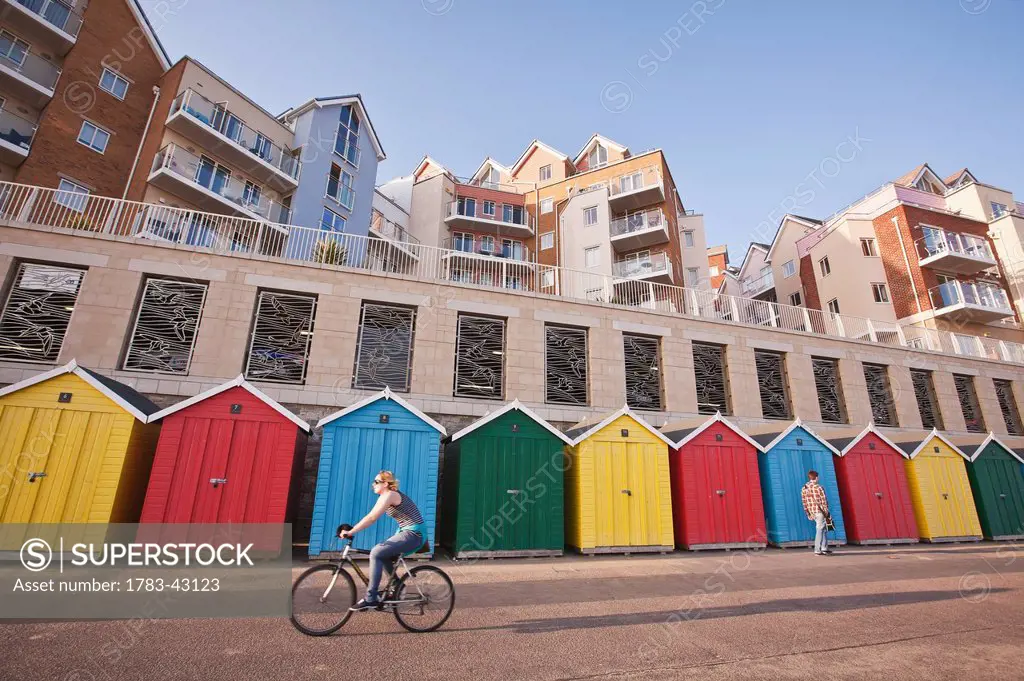 Cyclist, pedestrian, colorful beach huts and apartments at Honeycombe Beach development next to Boscombe Pier; Bournemouth, Dorset, England, UK