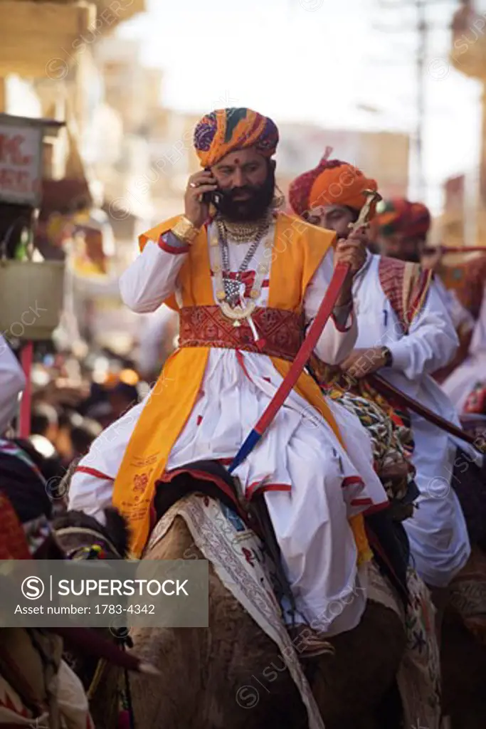 Man riding camel using cell phone at Jaisalmer festival, Rajasthan, India