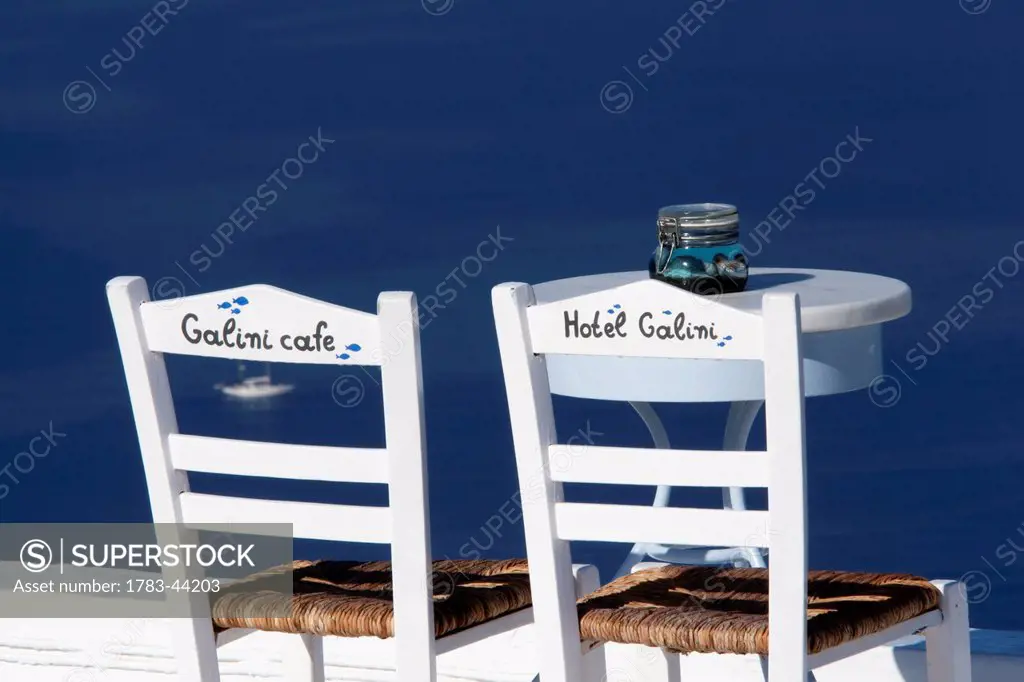 Chairs and a table on a patio overlooking the water from Hotel Galini and Galini Cafe; Firostefani, Santorini Island, Greece