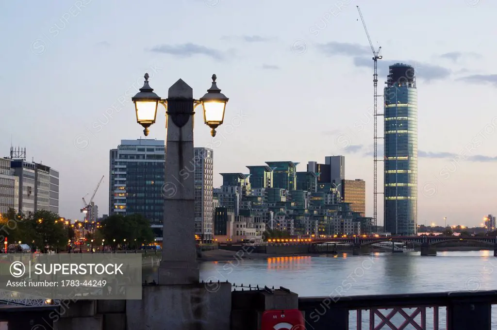 Lamp post illuminated at dusk and buildings along the waterfront; London, England