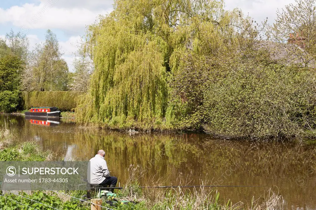 Fisherman fishing along banks of Kennet and Avon Canal; Hungerford, Berkshire, England