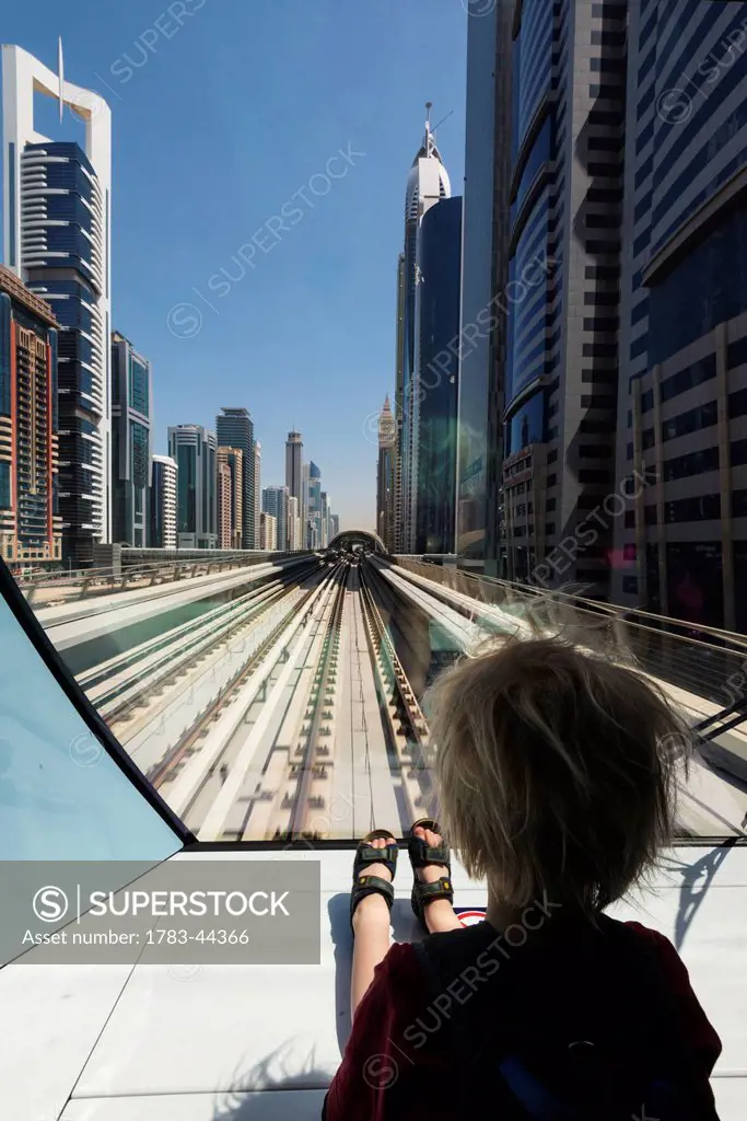 Young boy sitting at the front of metro train as it travels through the business district of Dubai; Dubai, United Arab Emirates