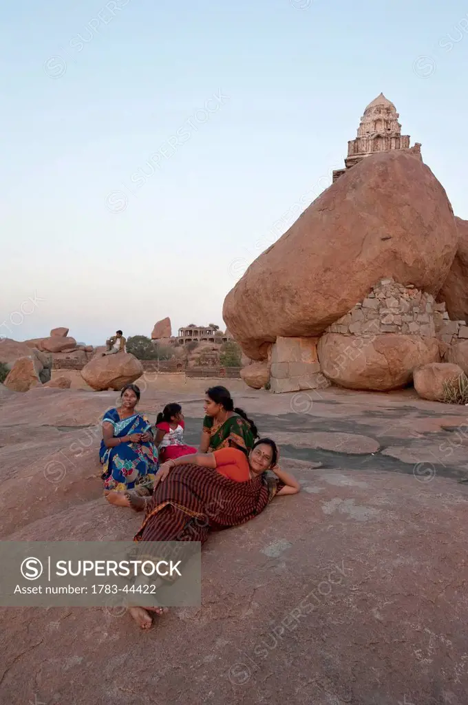 Three women and a girl sit on a rock surface overlooking the landscape; Hampi, Karnataka, India