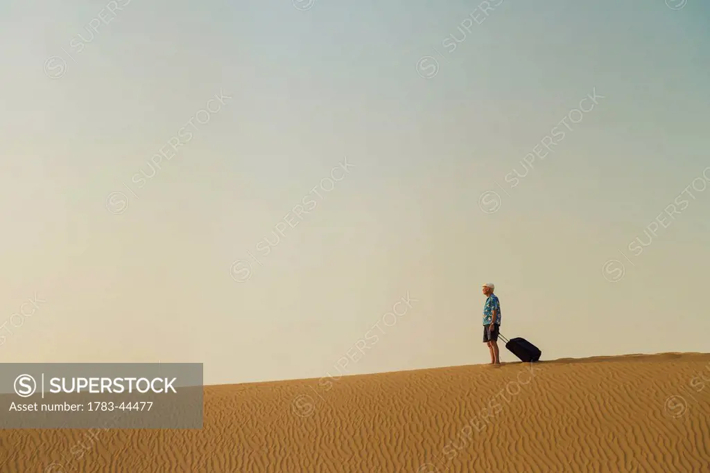 Barefoot man with suitcase on sand dune; Dubai, United Arab Emirates