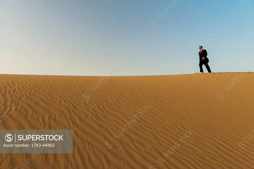 Man in smart suit walking along top of sand dune at dusk; Dubai, United Arab Emirates