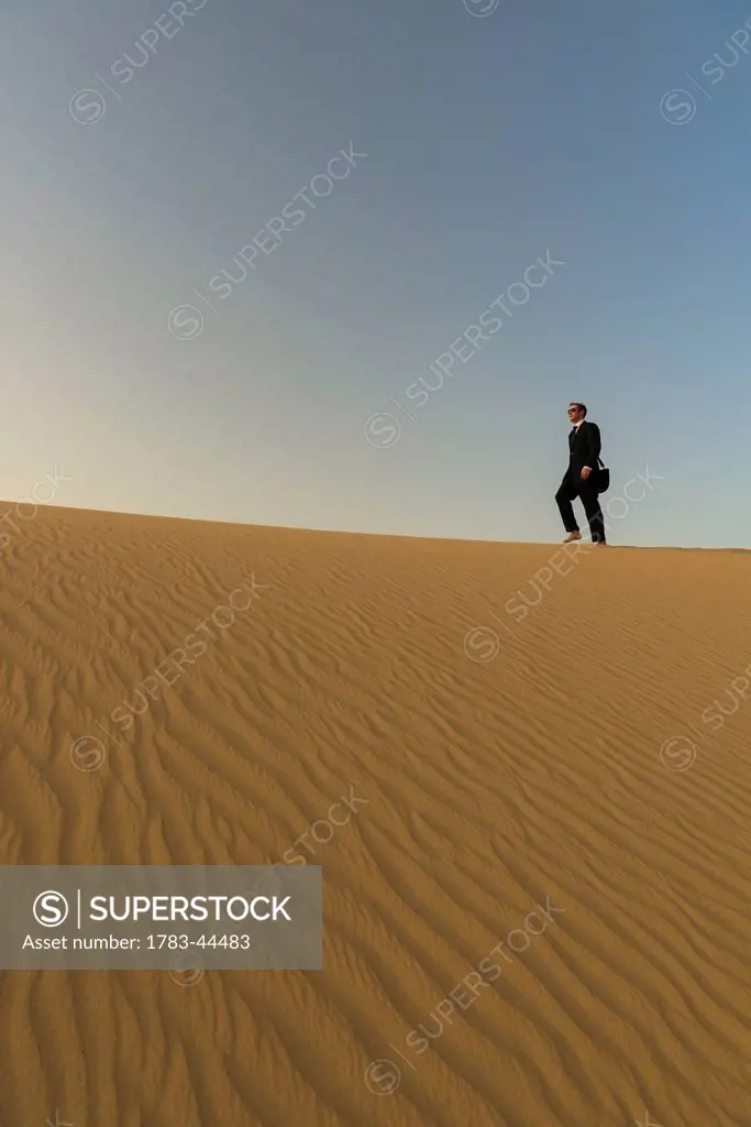 Man in smart suit walking along top of sand dune at dusk; Dubai, United Arab Emirates