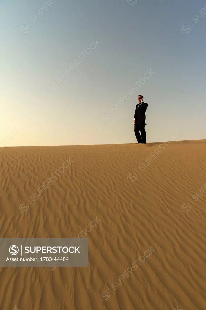 Man in smart suit making phone call on top of sand dune at dusk; Dubai, United Arab Emirates