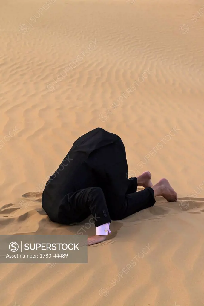 Man in smart suit with head buried in the sand; Dubai, United Arab Emirates