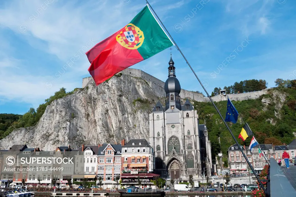 A church and other buildings along the water and flags flying; Dinant, Belgium