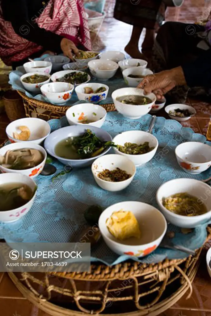Young woman traveller enjoying breakfast with elderly local women at temple, Bowls on tables in Vang Vieng,Laos