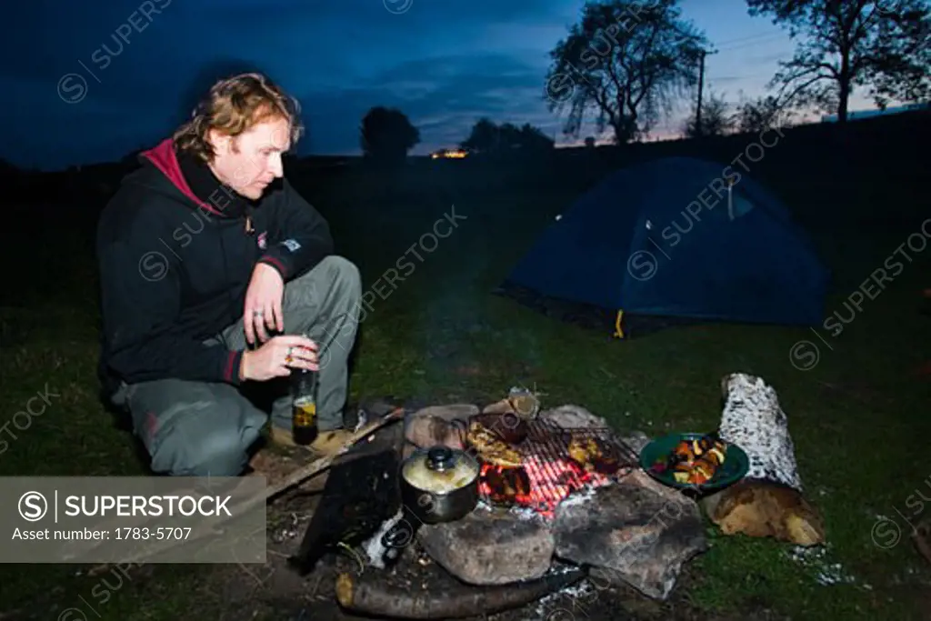 Man cooking over charcoal embers of wood fire, Dartmoor National Park,Postbridge,Yelverton,Devon,UK