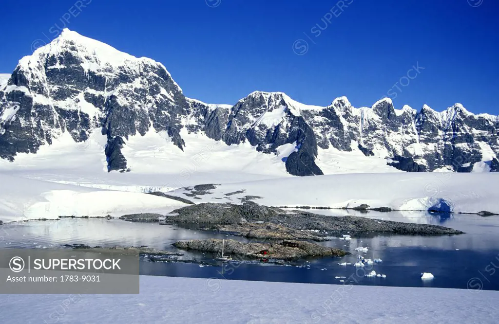 Tiny hut and boat and large mountains with snow, Port Lockroy, Antarctic Peninsula, Antarctica, The Arctic Circle