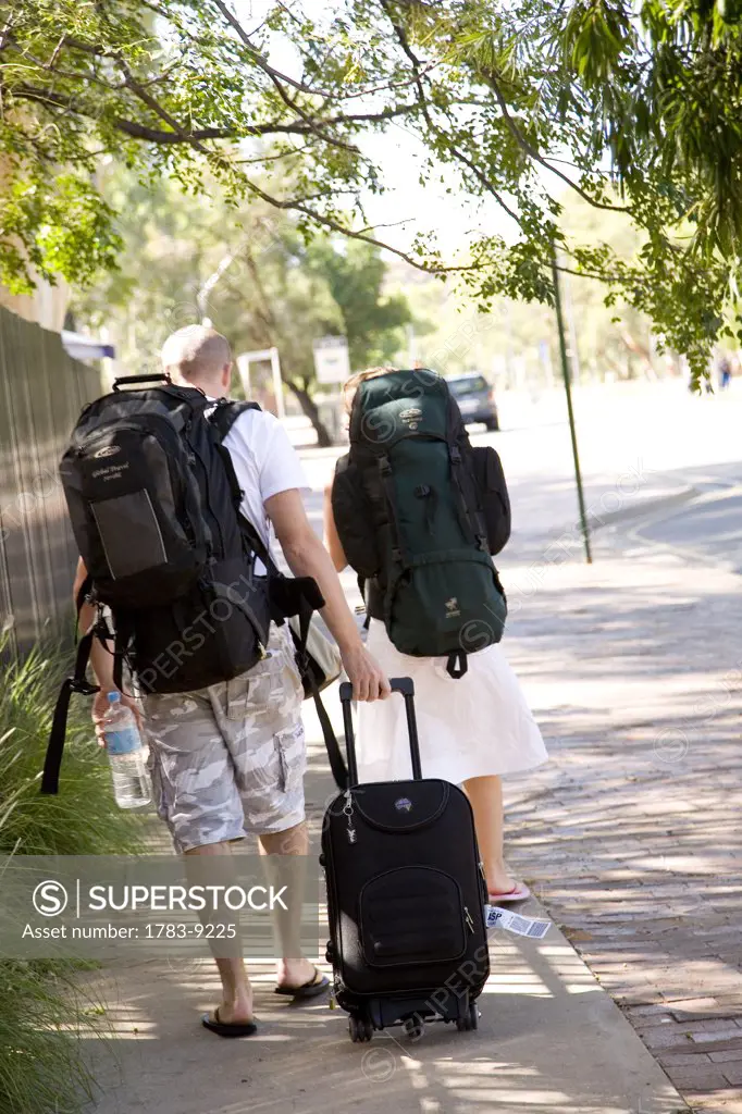 Young couple walking down  street with backpacks and suitcase, Alice Springs, Northern Territory, Australia